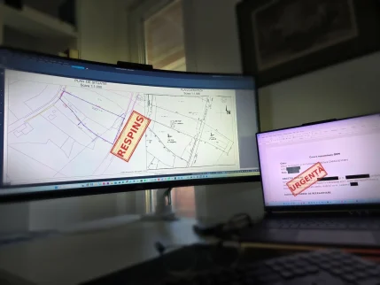 Plan De Situație Și Plan De Expertiză Deschise Pe Monitor, Cu Ștampila De Respins, Lângă Laptopul Cu Cererea De Reexaminare Adresată Ocpi